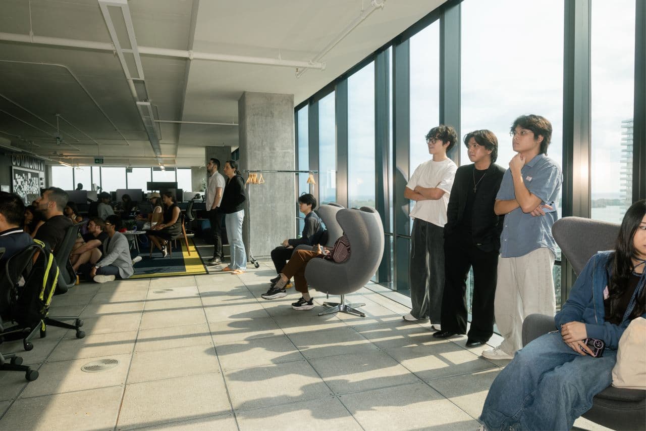 A packed session at Seneca Polytechnic, students watching a talk against floor-to-ceiling windows overlooking the Toronto lakefront.